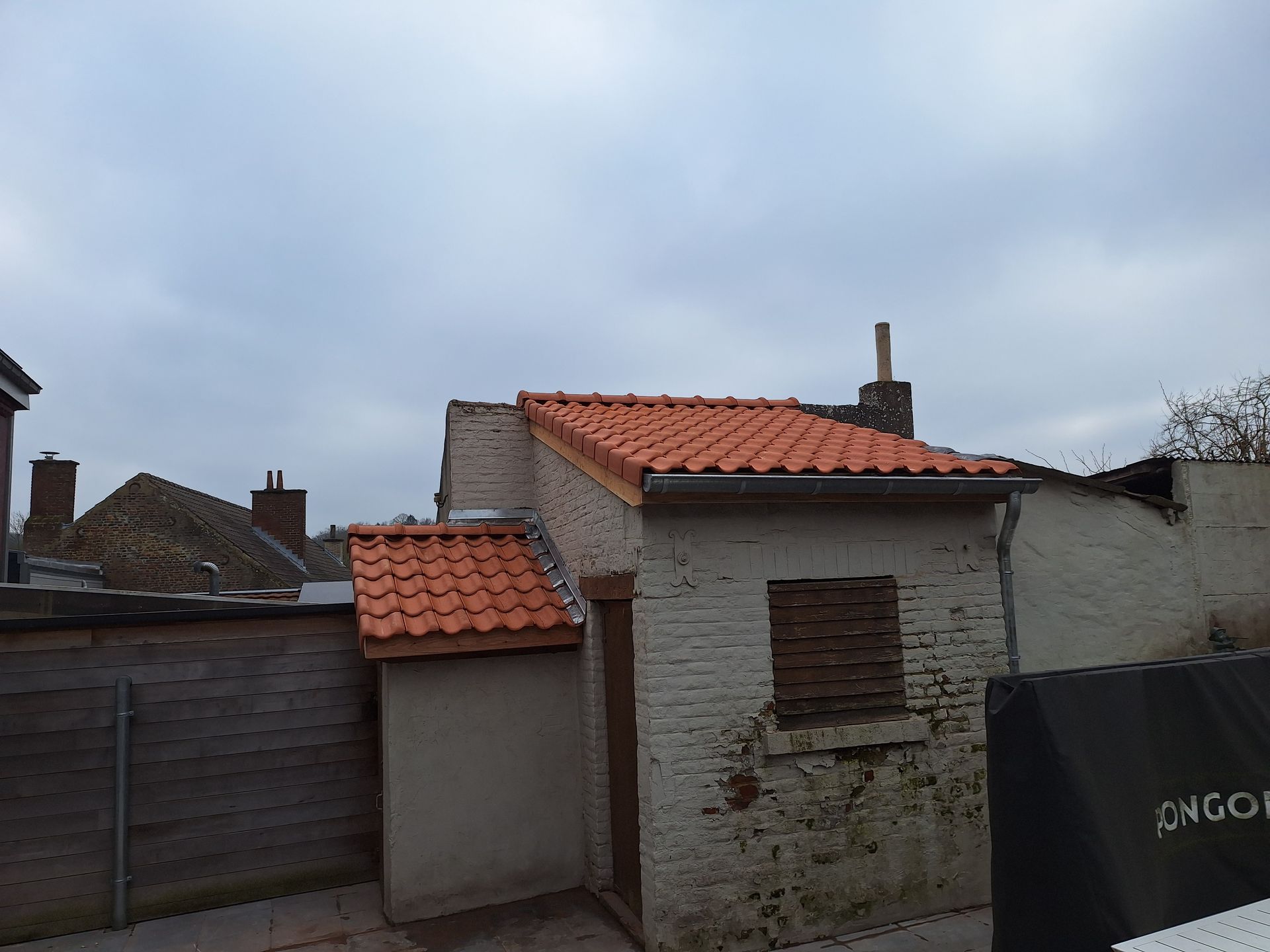 Rénovation de toiture en appentis avec tuiles terre cuite orange. Pose d'une gouttière pendante en zinc et d'une descente d'eaux pluviales. Finition de rive avec solins en plomb pour l'étanchéité contre le mur de façade d'une annexe ancienne.