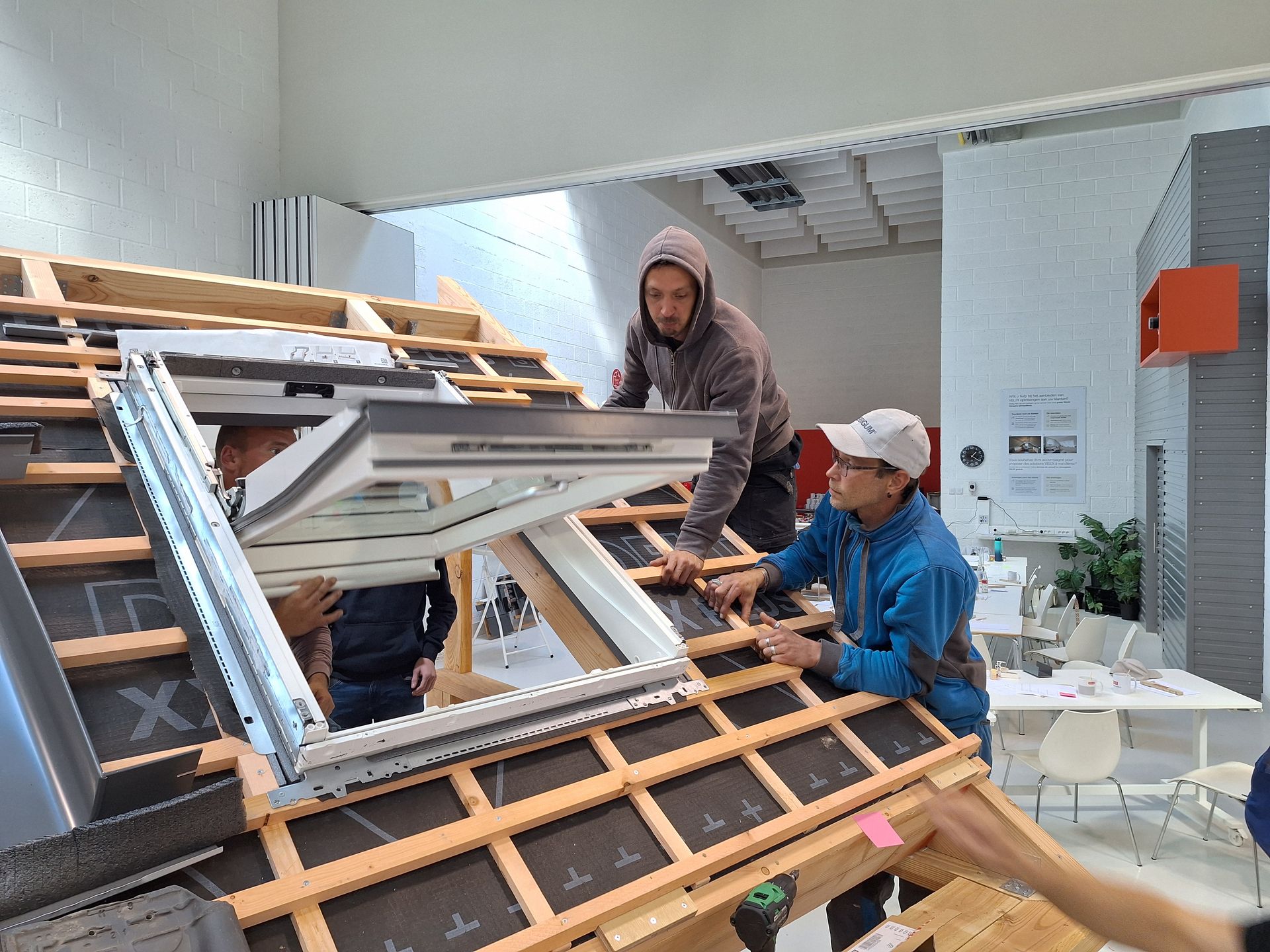 Formation technique à l'installation d'une fenêtre de toit Velux sur une structure bois. Mise en place du cadre isolant et raccord d'étanchéité sur lattes et contre-lattes avec écran de sous-toiture HPV. Équipe de couvreurs professionnels en plein montage de menuiserie de comble
